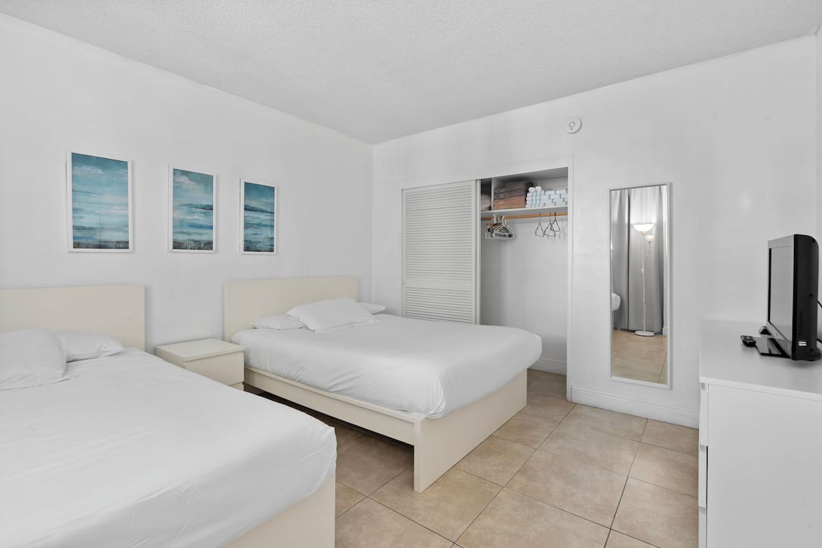 Habitación de hotel con dos camas, un armario, televisor y baño visible a través de una puerta.
