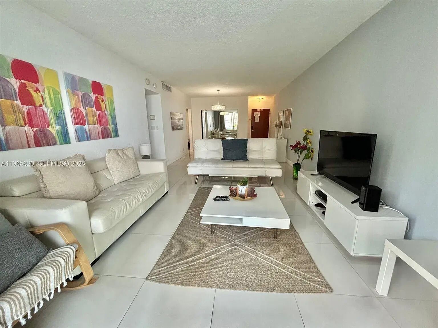 A modern living room with a sofa, coffee table, TV, and a colorful abstract painting on the wall.