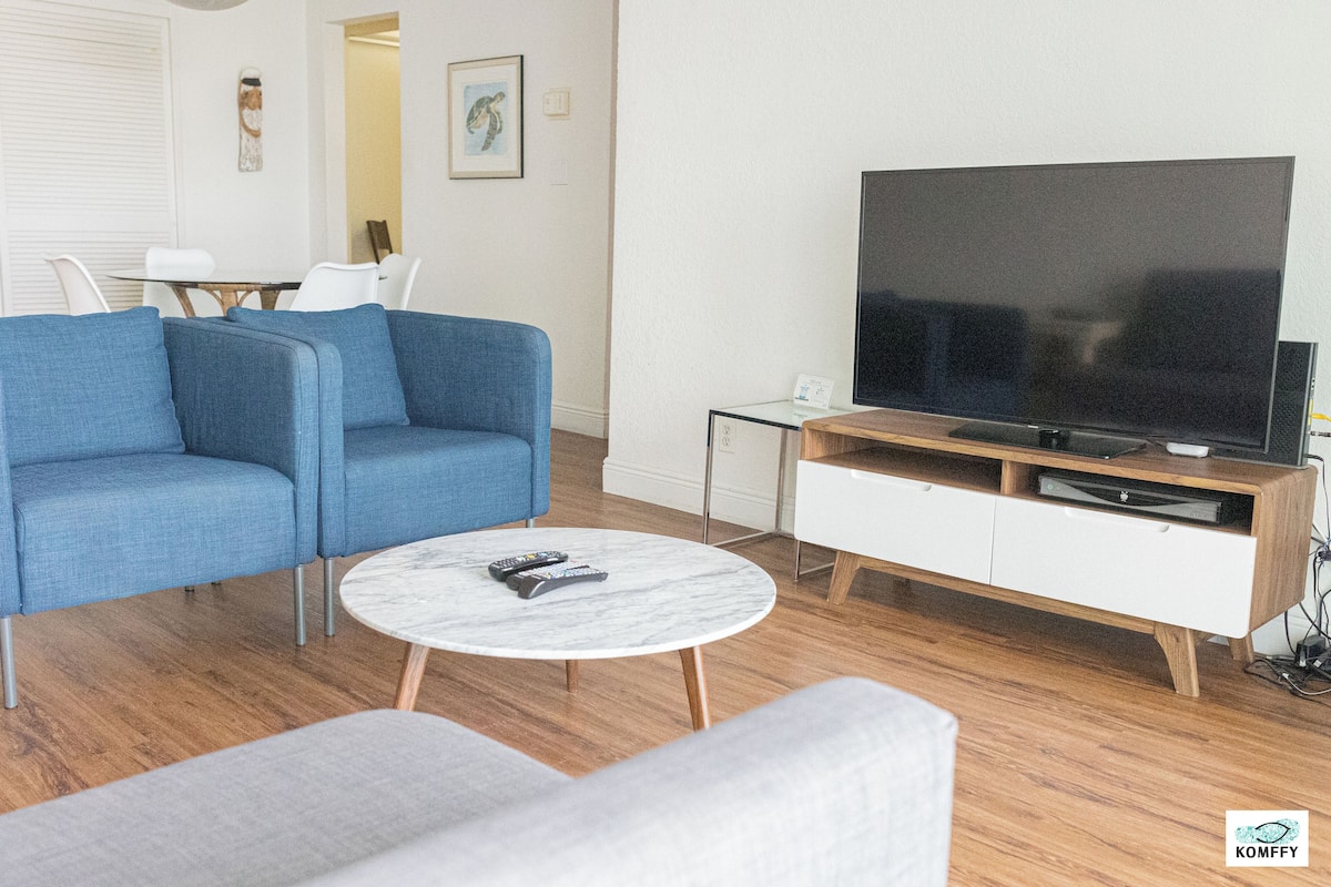 Una sala moderna con un sofá azul, una mesa de centro blanca y un televisor sobre un mueble de madera.
