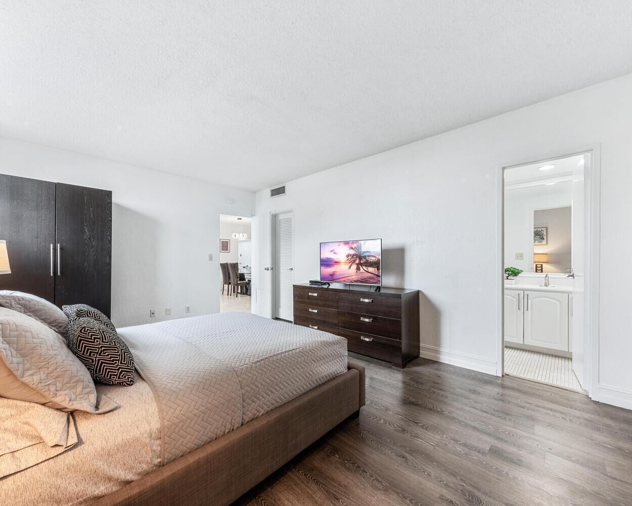 Una camera da letto moderna con un letto grande, una cassettiera in legno scuro e un televisore.