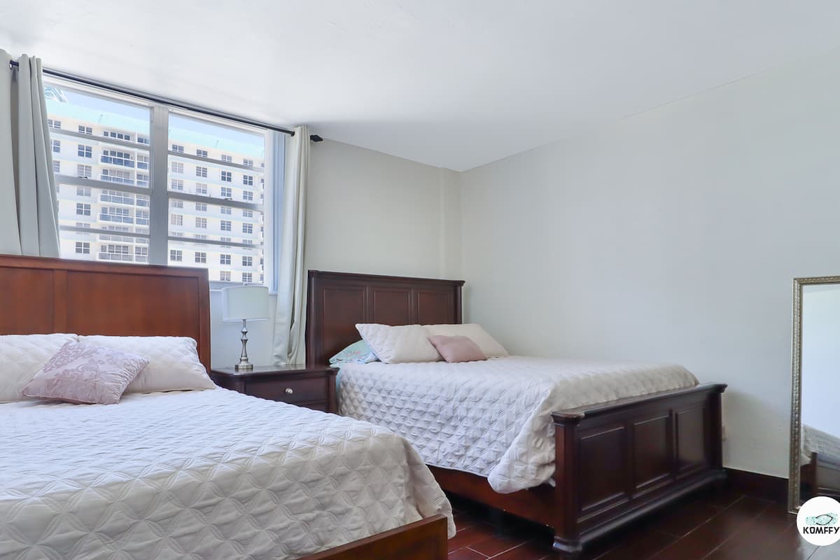 Habitación de hotel con dos camas, un ventanal grande y vistas a un edificio.