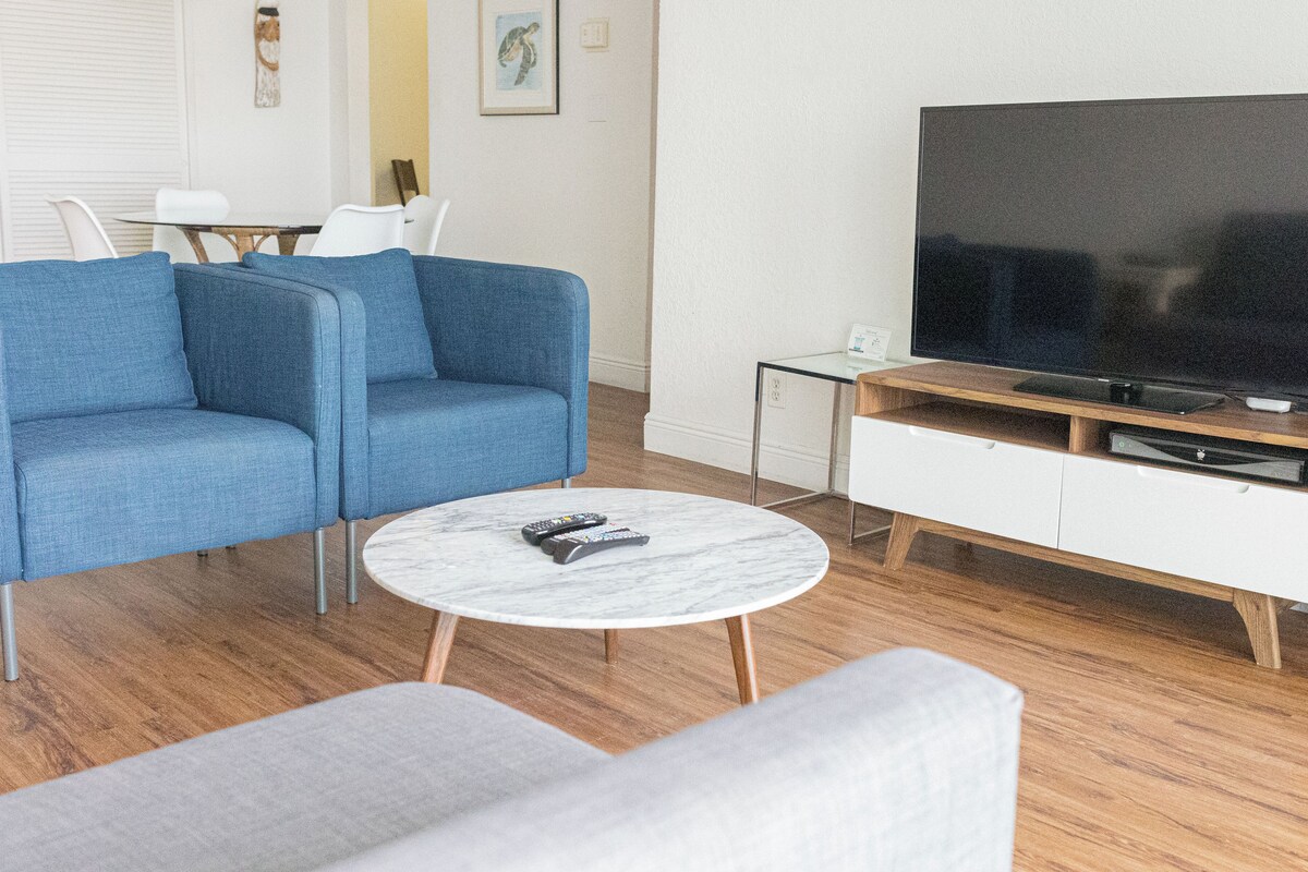 Una sala moderna con un sofá azul, una mesa de centro blanca y un televisor sobre un mueble de madera.