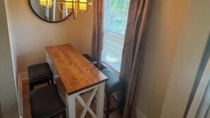 A compact dining area with a wooden table and two chairs, a round mirror on the wall, and a window with curtains.