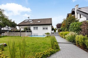 Une maison moderne à deux étages, dotée d’une piscine, d’une allée pavée et d’un jardin bien entretenu.
