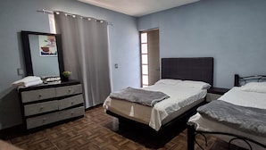 Une chambre avec deux lits, une commode, un miroir et une fenêtre avec des rideaux.