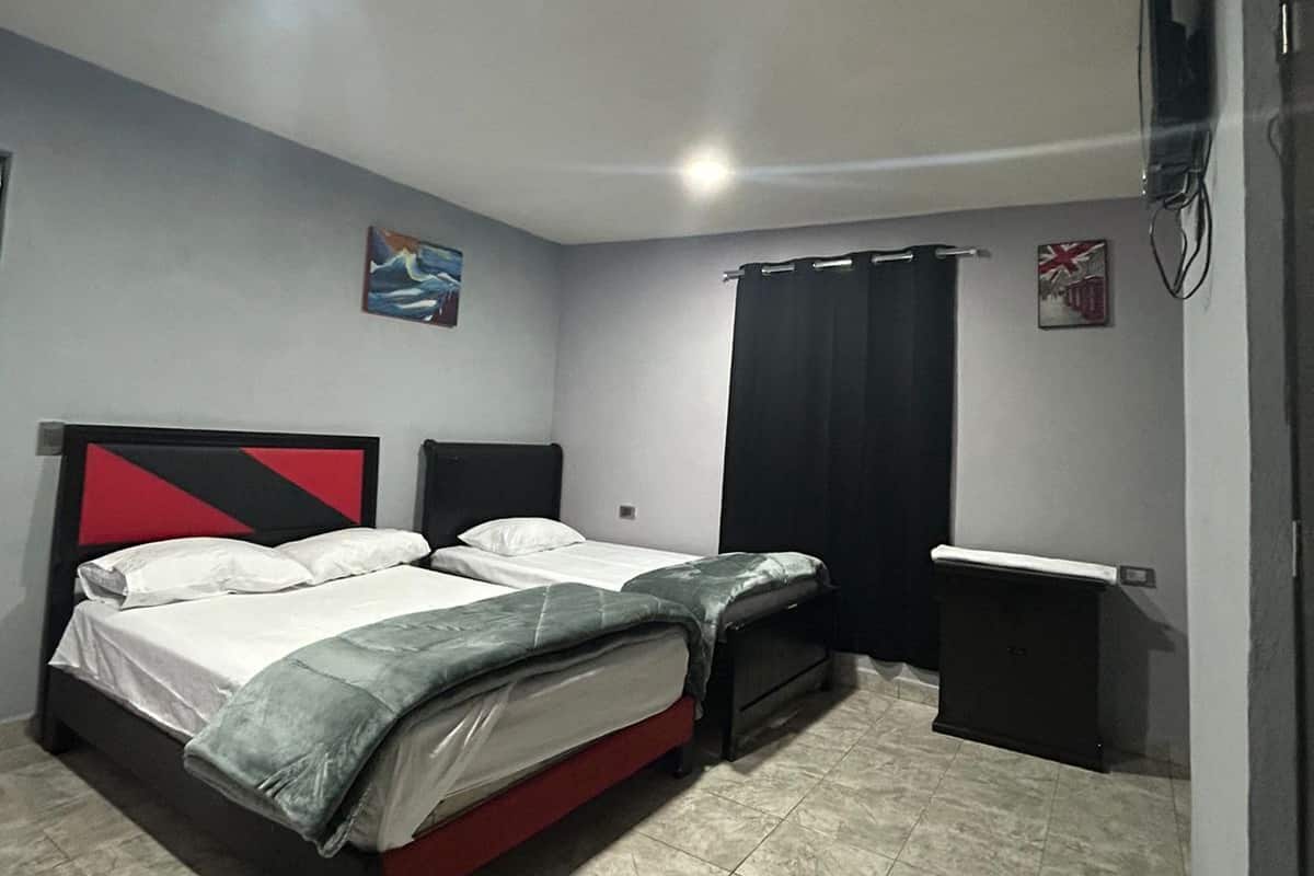 Un dormitorio con cama, mesita de noche, televisor de pared y ventana con cortinas.