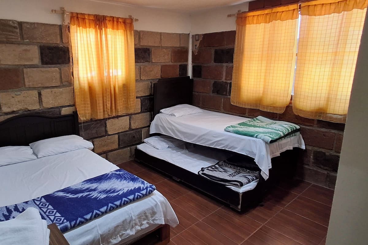 Una habitación con dos camas, una pared de piedra y cortinas.