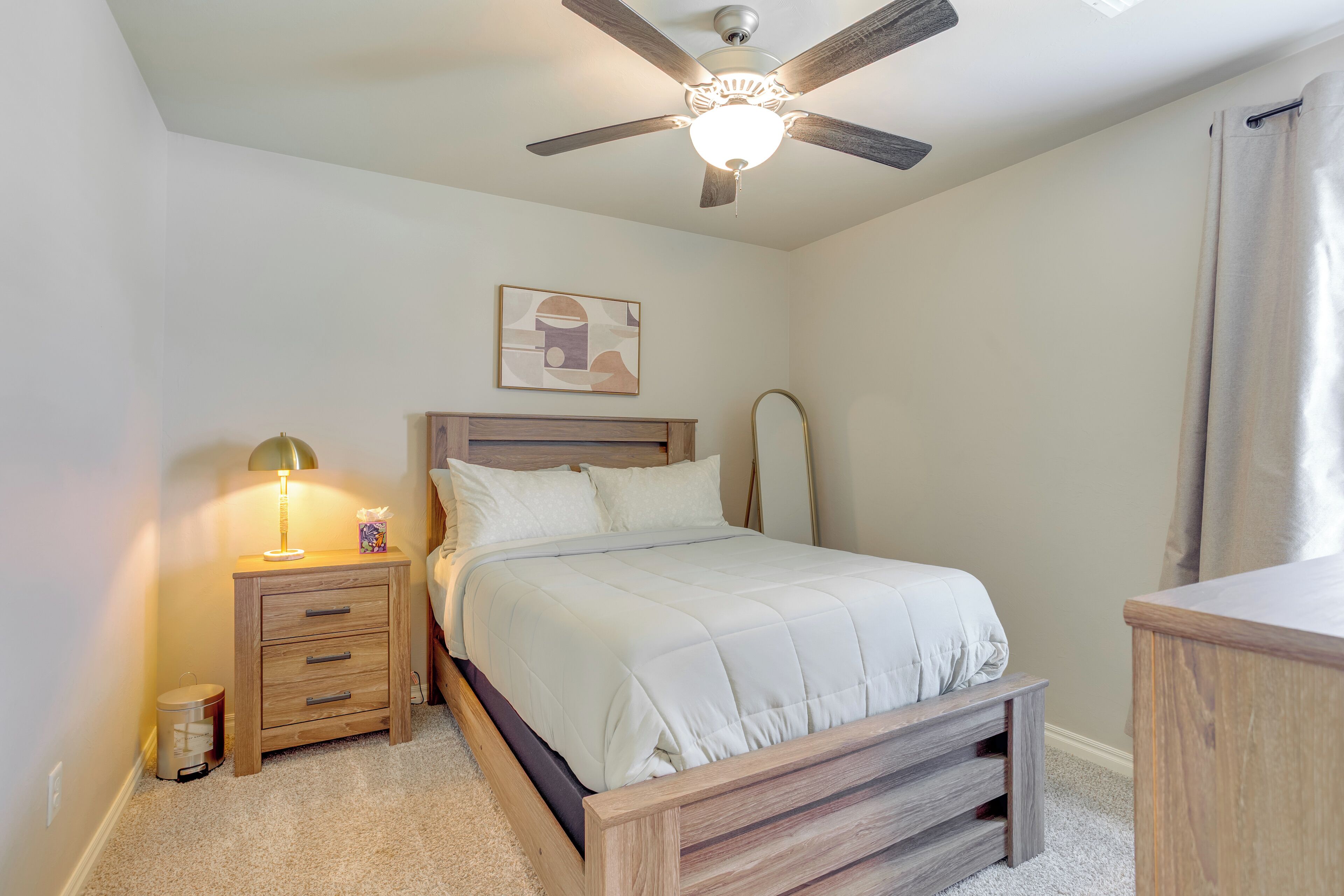 A bedroom with a bed, a nightstand with a lamp, a ceiling fan, and a wall-mounted artwork.
