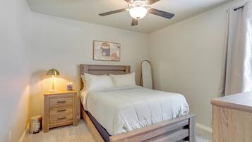 A bedroom with a bed, a nightstand with a lamp, a ceiling fan, and a wall-mounted artwork.