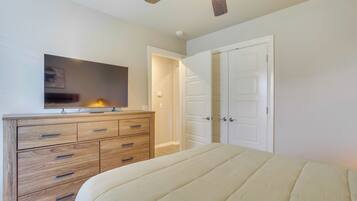 Une chambre à coucher comprenant un lit, une commode en bois, un ventilateur de plafond et un téléviseur fixé au mur.