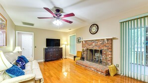Una sala de estar con chimenea, ventilador de techo, televisor y sofá.