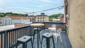 Un patio en la azotea con una mesa de madera y dos sillas, una mesita blanca y un taburete metálico.