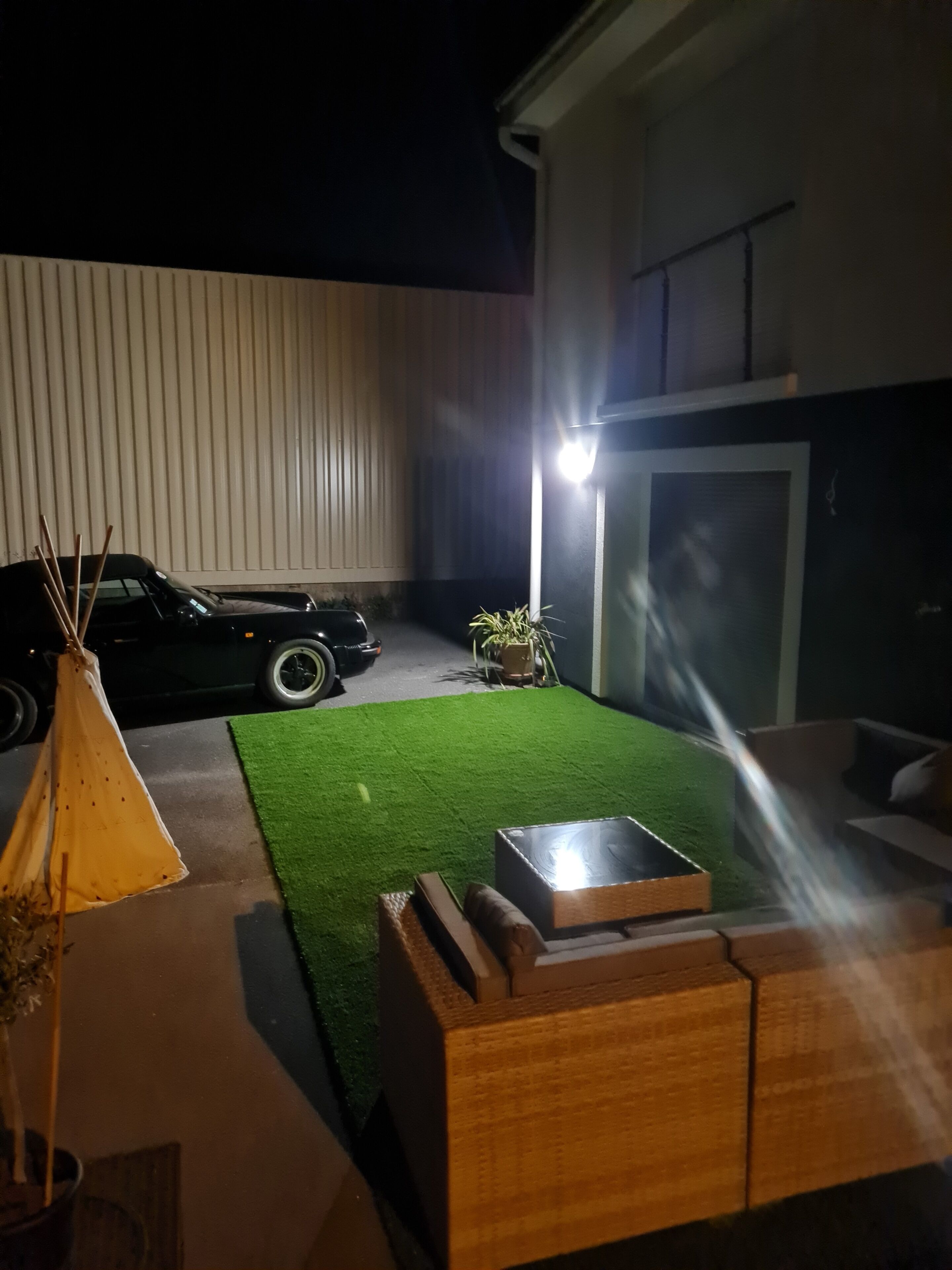 A modern outdoor space with a green artificial turf, a wooden bench, a black car, and a tent.
