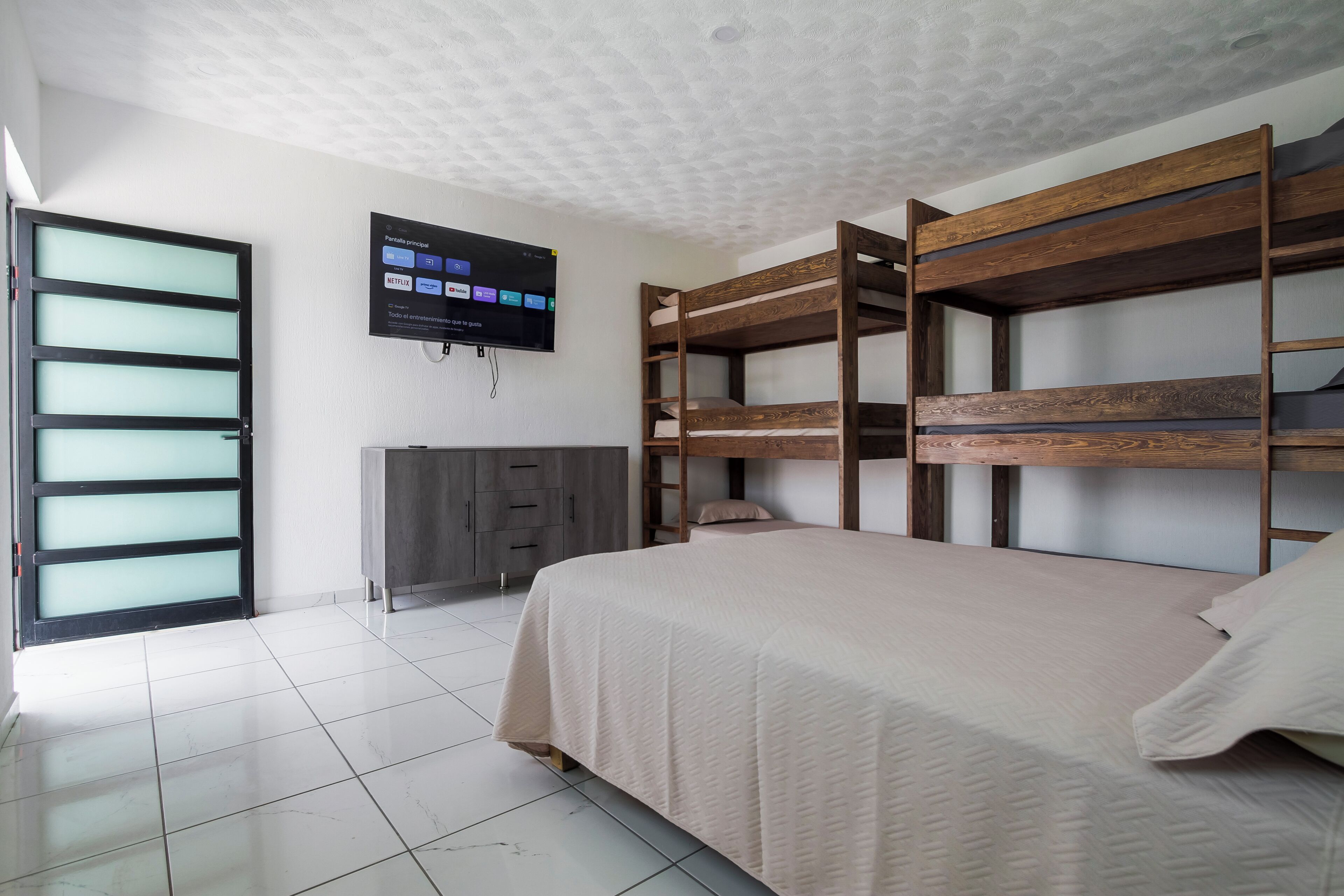 A room with bunk beds, a television mounted on the wall, a cabinet, and a sliding door.