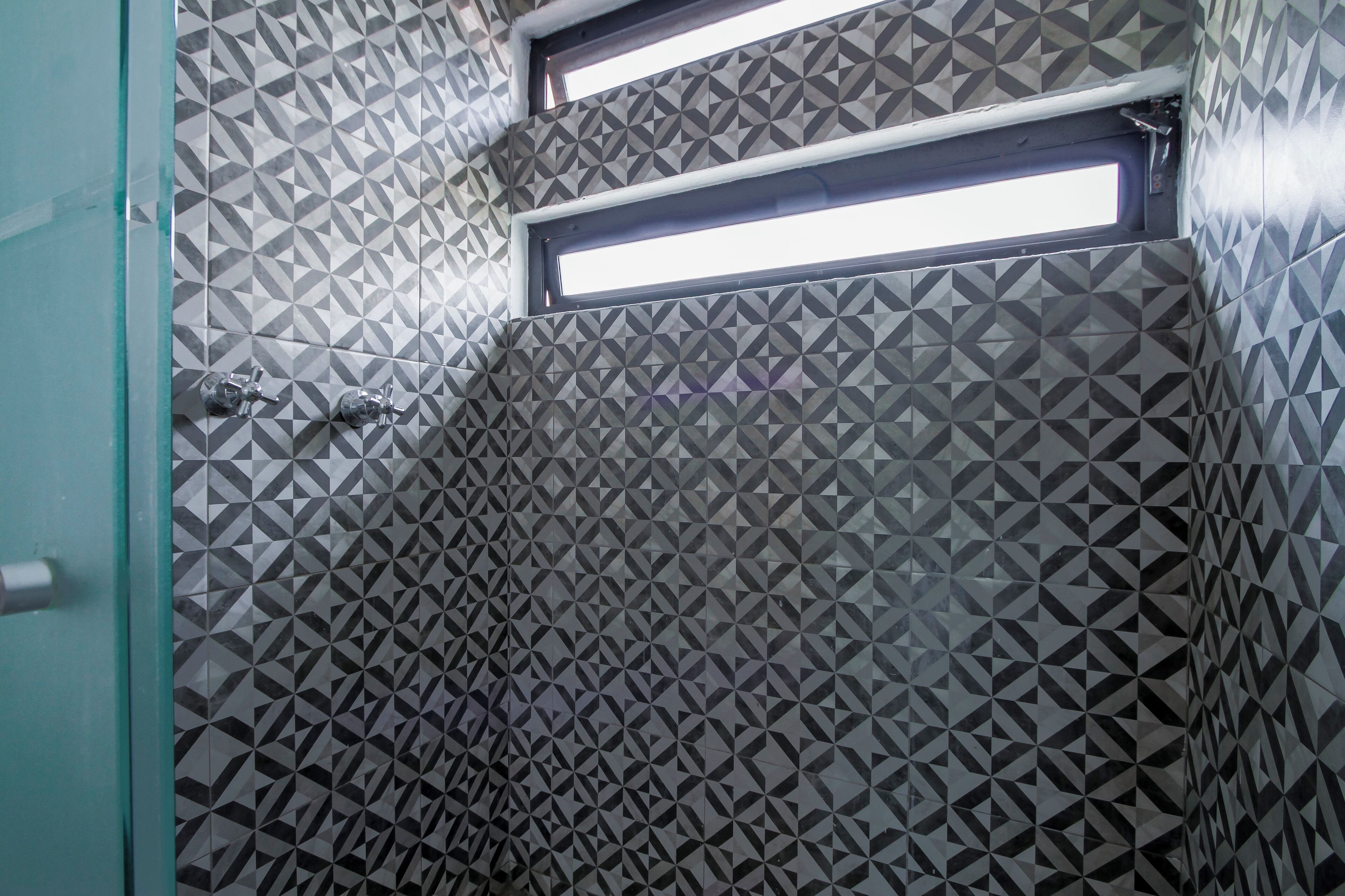 A bathroom with geometric patterned tiles, a window, and a glass door.
