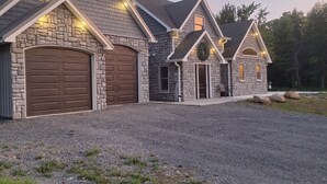 A two-story house with a stone facade, a large garage, and a gravel driveway. - Charming, quiet 1-bedroom house in welcoming Brockport (Brockport)