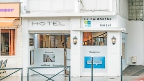 Fachada de hotel con letrero 'HOTEL', un cartel de 'BIENVENIDOS' en la entrada y una señalización que indica 'Recepción'.