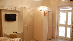 A room with a TV, a small desk, a wardrobe, and a dining table with chairs.