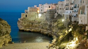 A coastal town with buildings built into the cliffside, overlooking a calm sea.