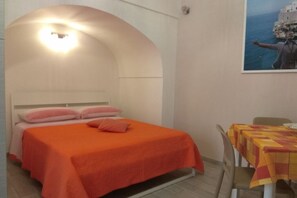 Um quarto com uma cama, teto em arco, uma mesa com toalha quadriculada e uma moldura na parede.