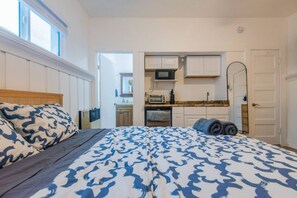 A bedroom with a bed, a nightstand, and a view of a kitchen area.