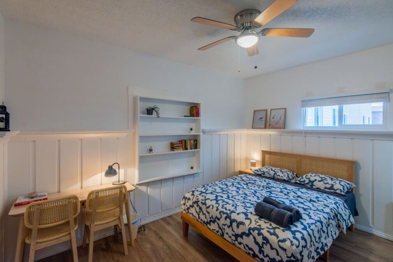 Una camera da letto con un letto, una scrivania con una sedia, una libreria e una ventola a soffitto.