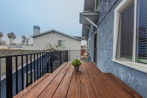 A wooden deck with a potted plant, a black railing, and a house with a white exterior and blue trim. - Broadway 8 - Clean Private Studio (Redondo Beach)