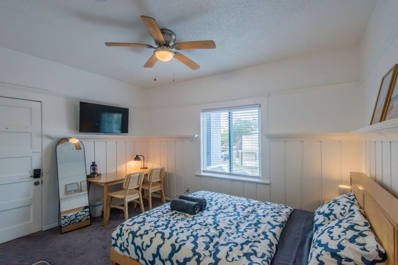 A bedroom with a bed, a desk, a chair, a television, and a window.