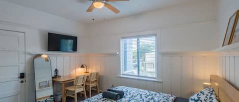 A bedroom with a bed, a desk, a chair, a television, and a window.