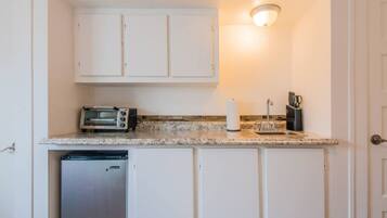 A compact kitchen with white cabinets, a built-in toaster, a sink, and a small refrigerator.