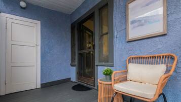 Een veranda met een rieten stoel, een kleine tafel met een plant en een lijst met een foto aan de muur.
