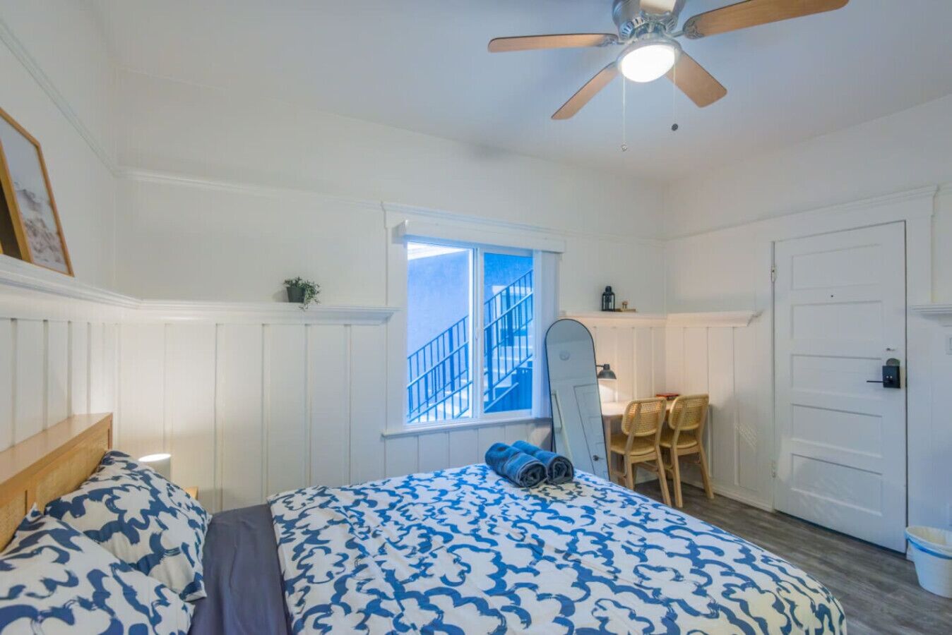 A bedroom with a bed, a ceiling fan, a window with a view of a staircase, and a door.