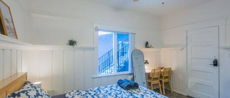 A bedroom with a bed, a ceiling fan, a window with a view of a staircase, and a door.