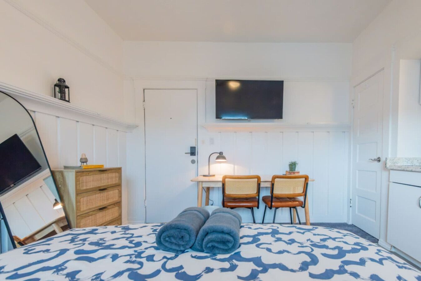 Un dormitorio con cama, dos sillas, un escritorio con lámpara, televisor y armario.