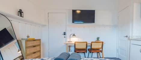 Un dormitorio con cama, dos sillas, un escritorio con lámpara, televisor y armario.