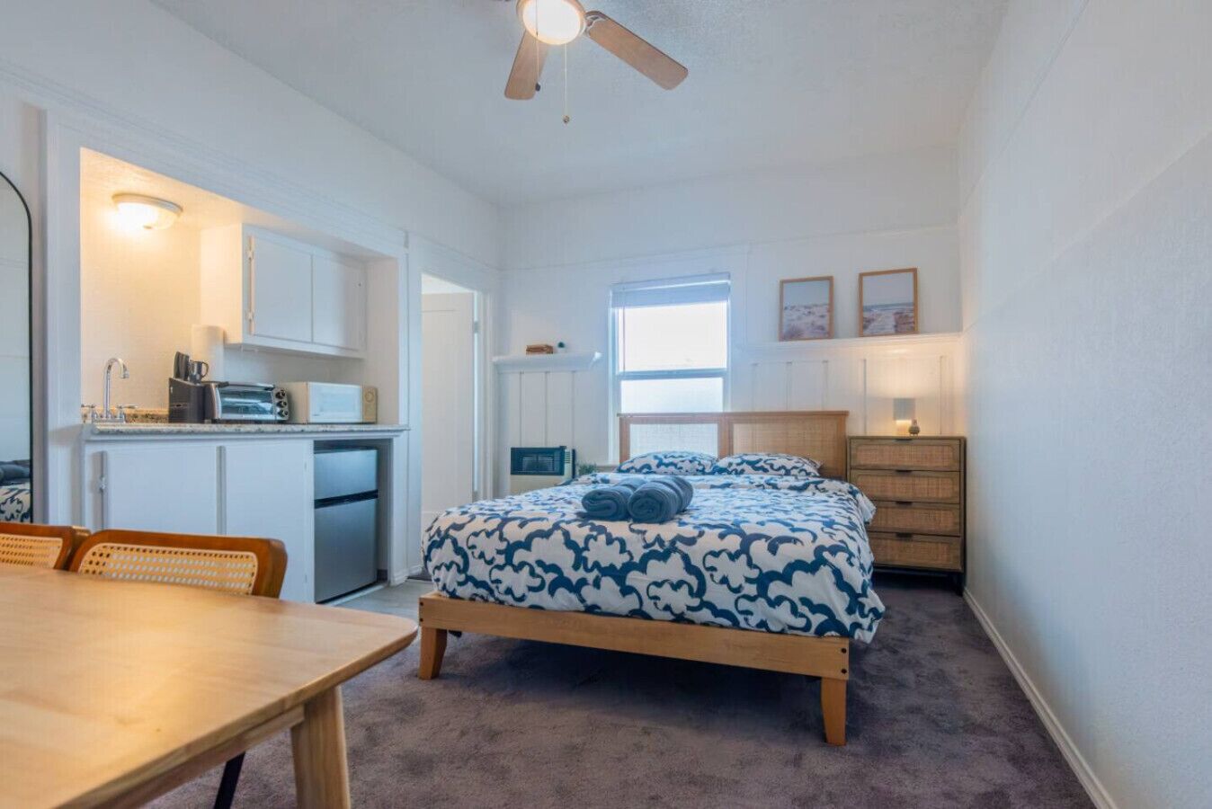A compact room with a bed, a small kitchenette, a dining area, and a window providing natural light.