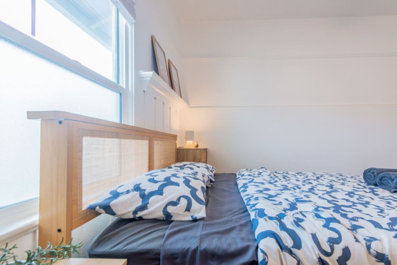 Une chambre avec deux lits, une fenêtre, une table de chevet et une étagère fixée au mur.