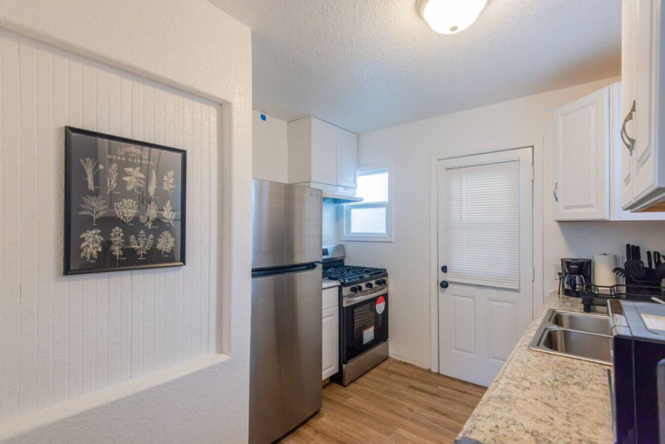 A compact kitchen with white cabinetry, a stainless steel refrigerator, a gas stove, and a built-in oven.