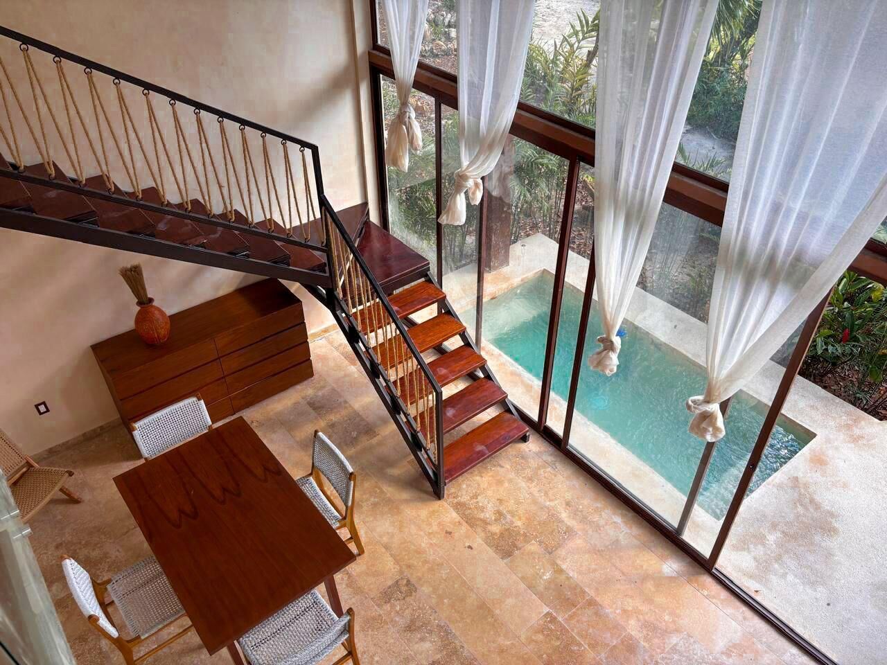 Una habitación amplia con una escalera de madera que da a un balcón con vistas a una piscina.
