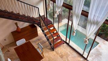 Una habitación amplia con una escalera de madera que da a un balcón con vistas a una piscina.