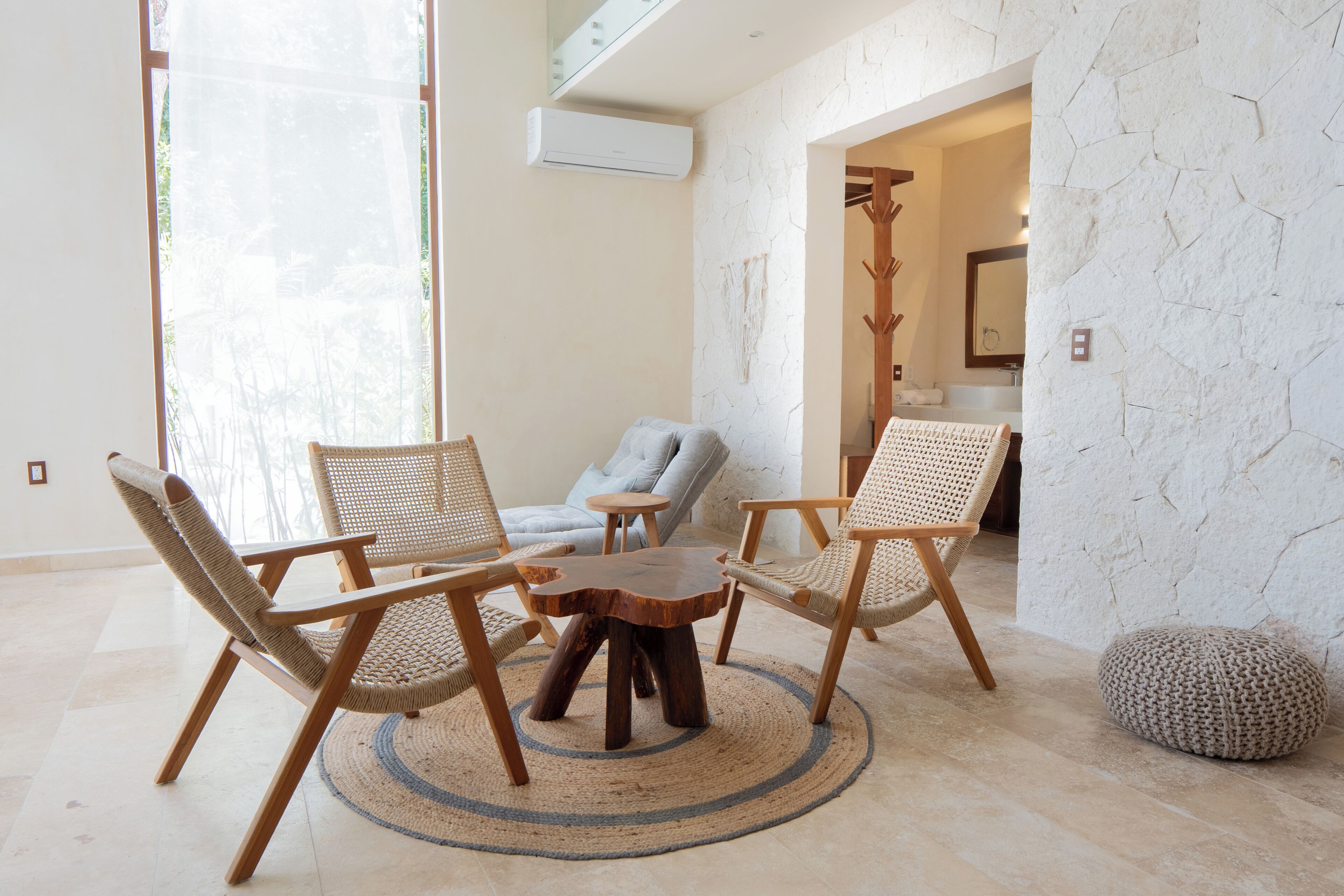 A room with a round wooden table surrounded by three woven chairs, a grey sofa, and a stone-textured wall.