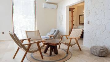 A room with a round wooden table surrounded by three woven chairs, a grey sofa, and a stone-textured wall.