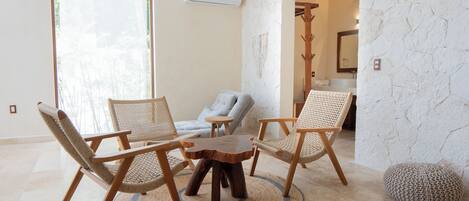 A room with a round wooden table surrounded by three woven chairs, a grey sofa, and a stone-textured wall.