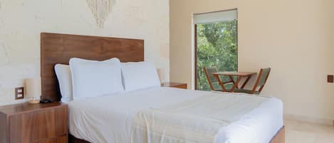 A bedroom with a wooden bed, a nightstand, a chair, and a window with a view of greenery.