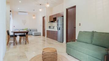 Una sala de estar moderna con un sofá verde, un comedor con mesa y sillas, y una cocina con refrigerador.