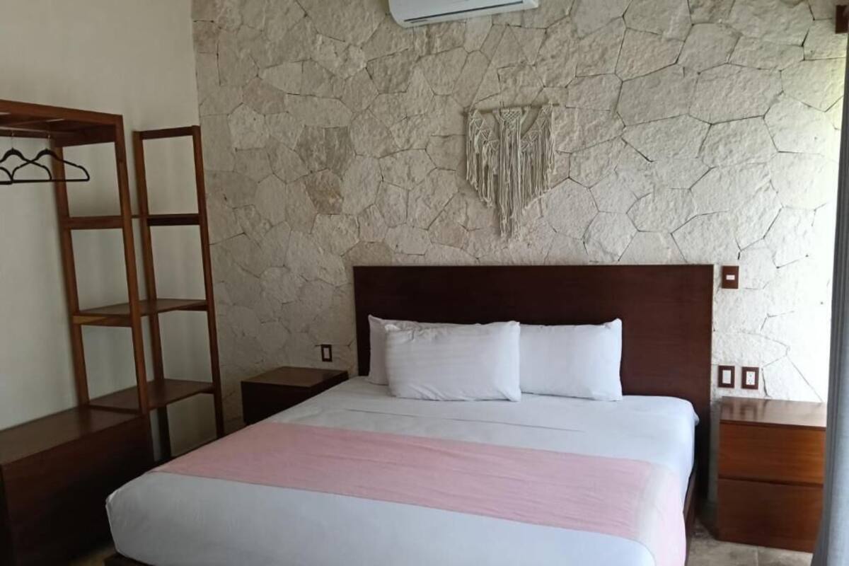 A bedroom with a bed, wooden nightstands, a wardrobe, and a stone wall.