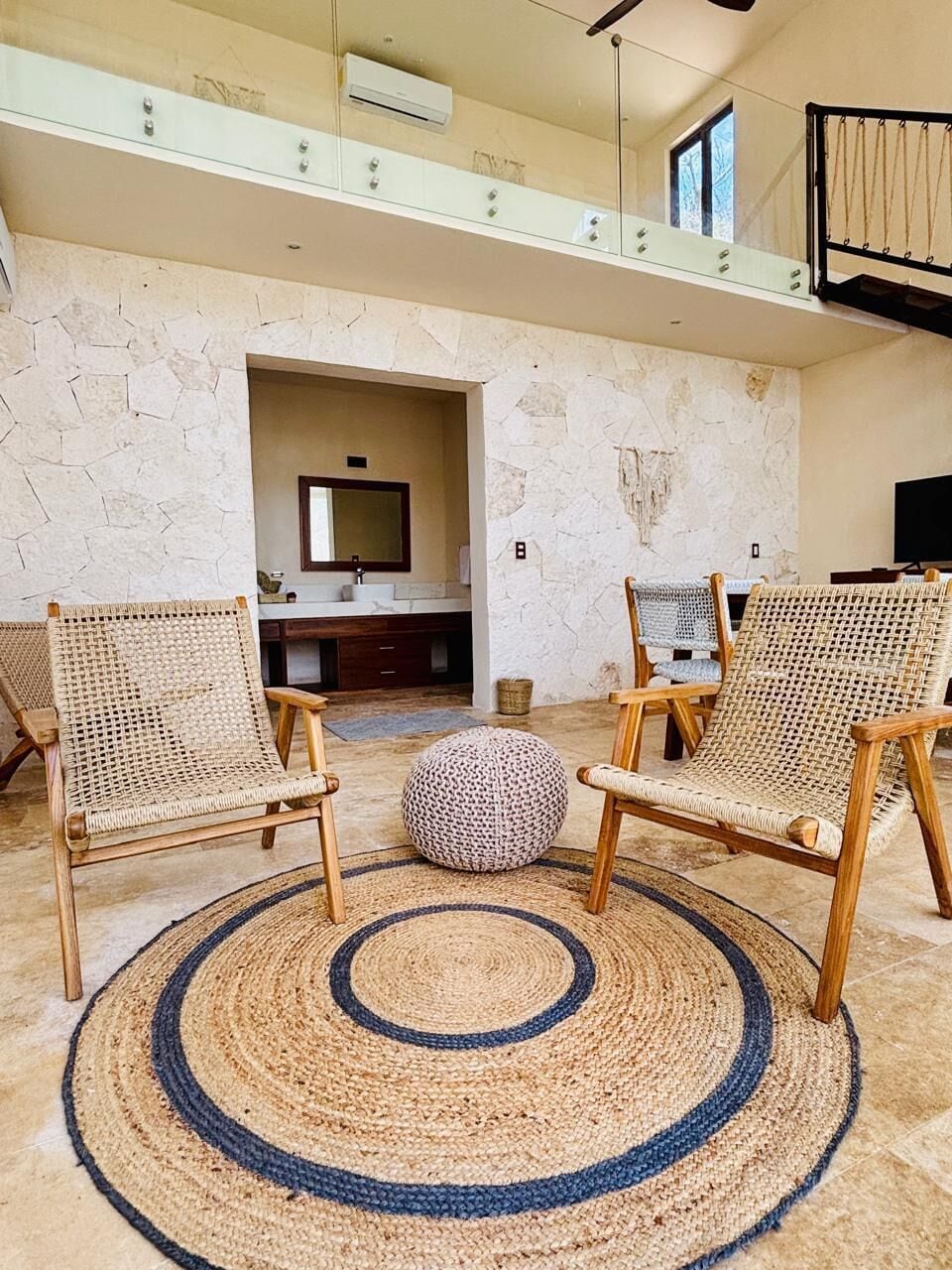 A spacious living area with two wicker chairs, a round woven rug, and a stone wall.