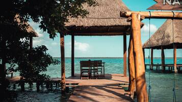 A wooden pier leading to a thatched-roof structure with a bench.