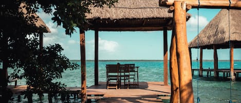 A wooden pier leading to a thatched-roof structure with a bench.