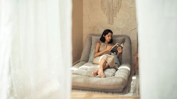 A person sitting on a sofa with a book, in a room with a textured wall and a curtain.